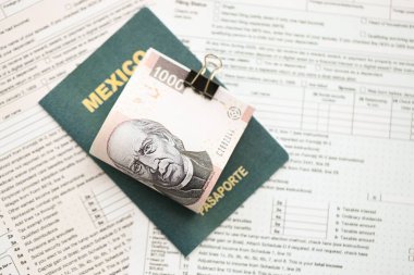 Meksika Pezosu 'nun büyük meblağlı para faturaları pasaport ve vergi formlarıyla birlikte masanın üzerinde duruyor. Maliye ve vergi ödeme kavramı