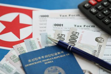 Kuzey Kore büyük miktarlarda para kazandı. Masada kalem, hesap makinesi, pasaport ve vergi formları var. Vergi ödeme ve muhasebe kavramı