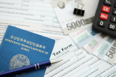 Kuzey Kore büyük miktarlarda para kazandı. Masada kalem, hesap makinesi, pasaport ve vergi formları var. Vergi ödeme ve muhasebe kavramı