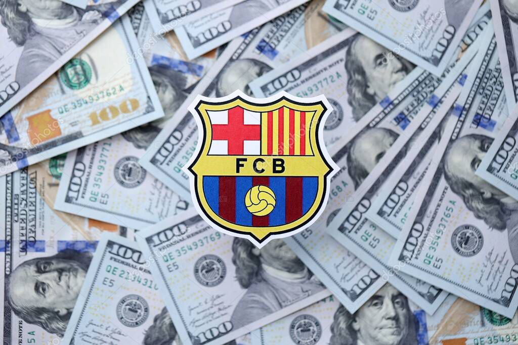 KYIV, UKRAINE - FEBRUARY 23, 2025 FC Barcelona football club badge lies on big amount of hundred US dollar bills