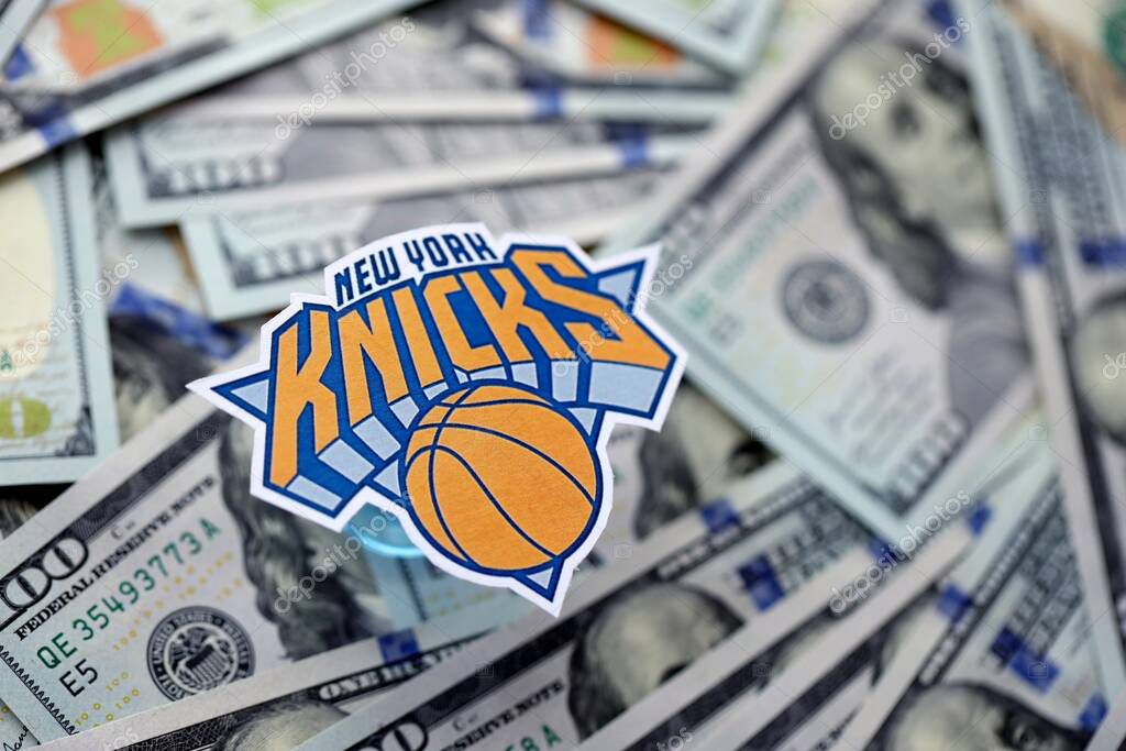KYIV, UKRAINE - FEBRUARY 23, 2025 New York Knicks basketball team badge lies on big amount of hundred US dollar bills close up