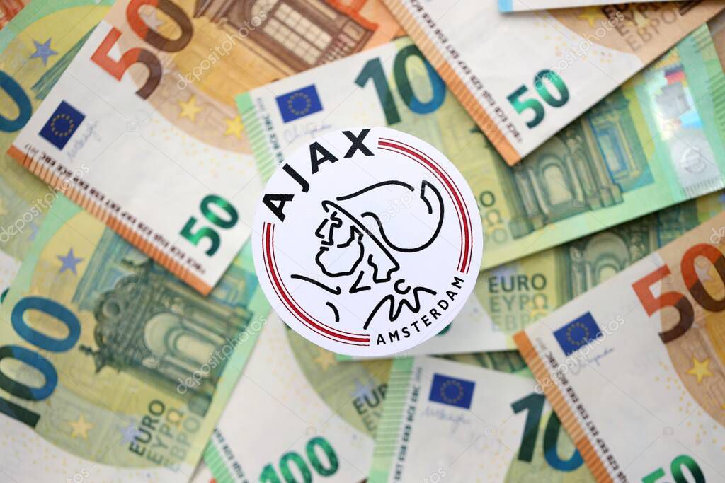 KYIV, UKRAINE - FEBRUARY 23, 2025 AFC Ajax football club badge lies on big amount of hundred EURO money bills