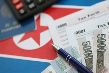 Kuzey Kore büyük miktarlarda para kazandı. Masada kalem, hesap makinesi, pasaport ve vergi formları var. Vergi ödeme ve muhasebe kavramı