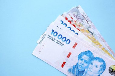 Arjantin Pezosu 'nun büyük miktarlarda para banknotları yakın planda, deniz mavisi renkli masada yatıyor. Finans ve bankacılık kavramı