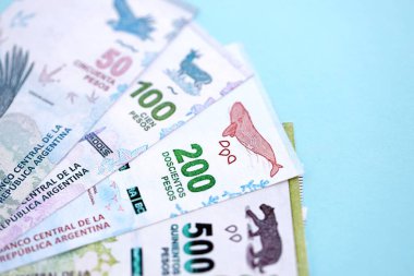 Arjantin Pezosu 'nun büyük miktarlarda para banknotları yakın planda, deniz mavisi renkli masada yatıyor. Finans ve bankacılık kavramı