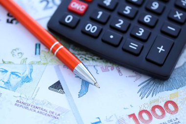 Arjantin Pezosu 'nun büyük miktarlarda para banknotları kalem ve hesap makinesiyle masanın üzerinde duruyor. Maliye ve vergi ödeme kavramı