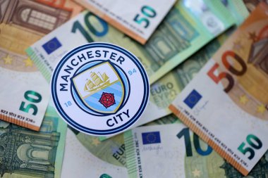 KYIV, UKRAINE - 23 Şubat 2025 Manchester City FC futbol kulübü rozeti büyük miktarda EURO para banknotlarının üzerinde yatıyor