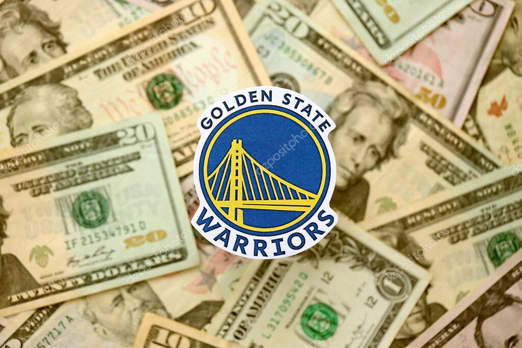 KYIV, UKRAINE - FEBRUARY 23, 2025 Golden State Warriors basketball team badge lies on big amount of US dollar bills close up