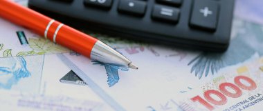 Arjantin Pezosu 'nun büyük miktarlarda para banknotları kalem ve hesap makinesiyle masanın üzerinde duruyor. Maliye ve vergi ödeme kavramı