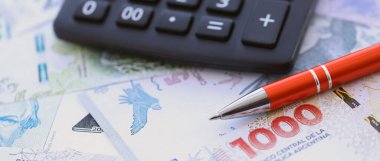 Arjantin Pezosu 'nun büyük miktarlarda para banknotları kalem ve hesap makinesiyle masanın üzerinde duruyor. Maliye ve vergi ödeme kavramı