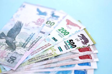 Arjantin Pezosu 'nun büyük miktarlarda para banknotları yakın planda, deniz mavisi renkli masada yatıyor. Finans ve bankacılık kavramı