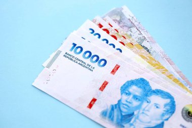 Arjantin Pezosu 'nun büyük miktarlarda para banknotları yakın planda, deniz mavisi renkli masada yatıyor. Finans ve bankacılık kavramı