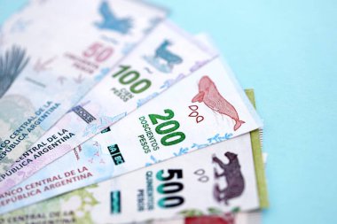 Arjantin Pezosu 'nun büyük miktarlarda para banknotları yakın planda, deniz mavisi renkli masada yatıyor. Finans ve bankacılık kavramı