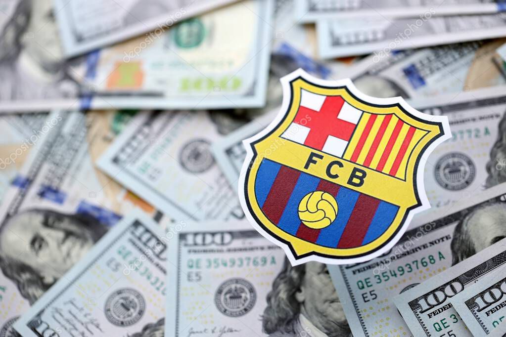 KYIV, UKRAINE - FEBRUARY 23, 2025 FC Barcelona football club badge lies on big amount of hundred US dollar bills