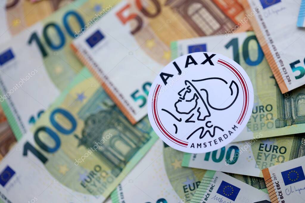 KYIV, UKRAINE - FEBRUARY 23, 2025 AFC Ajax football club badge lies on big amount of hundred EURO money bills
