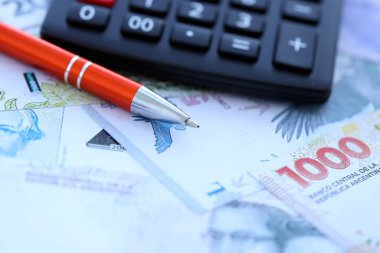 Arjantin Pezosu 'nun büyük miktarlarda para banknotları kalem ve hesap makinesiyle masanın üzerinde duruyor. Maliye ve vergi ödeme kavramı