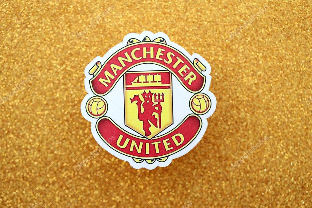 KYIV, UKRAINE - FEBRUARY 23, 2025 Manchester United FC football club badge lies on golden yellow glitter background banner
