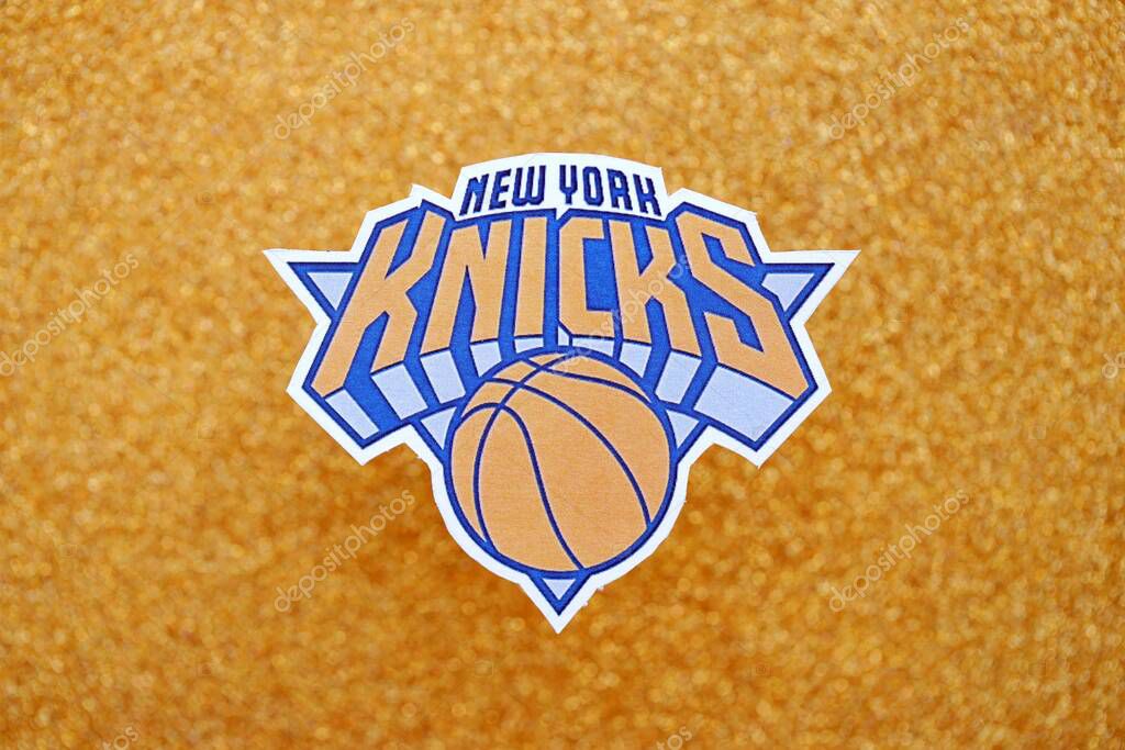KYIV, UKRAINE - FEBRUARY 23, 2025 New York Knicks basketball team badge lies on golden yellow glitter background banner