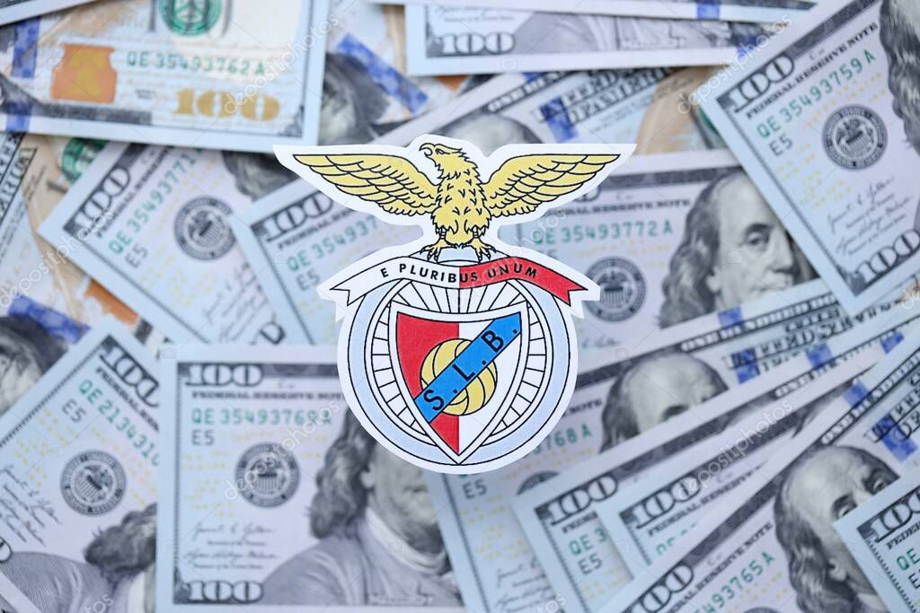 KYIV, UKRAINE - FEBRUARY 23, 2025 Sport Lisboa e Benfica football club badge lies on big amount of hundred US dollar bills