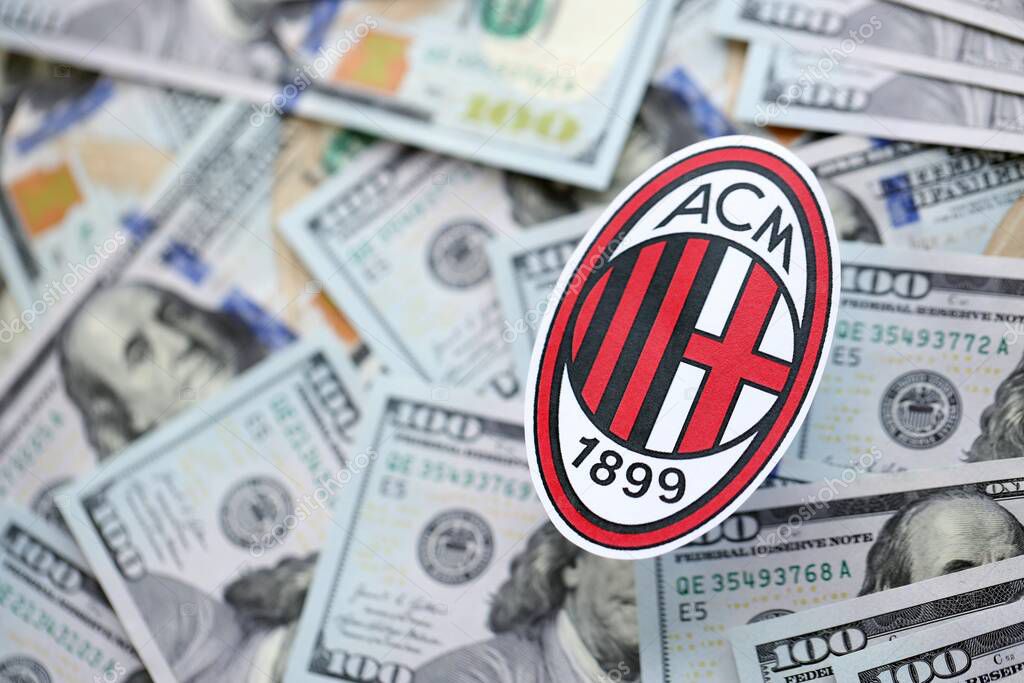 KYIV, UKRAINE - FEBRUARY 23, 2025 AC Milan football club badge lies on big amount of hundred US dollar bills