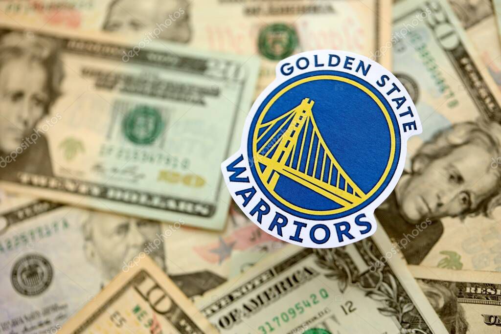KYIV, UKRAINE - FEBRUARY 23, 2025 Golden State Warriors basketball team badge lies on big amount of US dollar bills close up