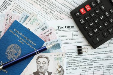 Kuzey Kore büyük miktarlarda para kazandı. Masada kalem, hesap makinesi, pasaport ve vergi formları var. Vergi ödeme ve muhasebe kavramı