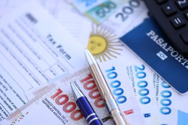 Arjantin Pezosu 'nun para faturaları kalem, hesap makinesi, pasaport ve vergi formlarıyla dolu. Finans ve bankacılık kavramı