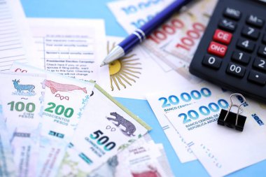 Arjantin Pezosu 'nun para faturaları kalem, hesap makinesi, pasaport ve vergi formlarıyla dolu. Finans ve bankacılık kavramı