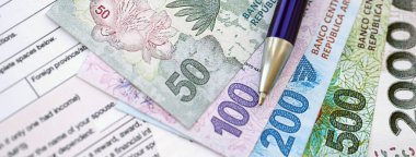 Arjantin pezosu. Büyük miktarda para. Masada, kalem ve vergi formları var.