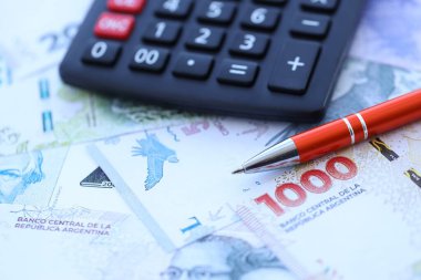 Arjantin Pezosu 'nun büyük miktarlarda para banknotları kalem ve hesap makinesiyle masanın üzerinde duruyor. Maliye ve vergi ödeme kavramı