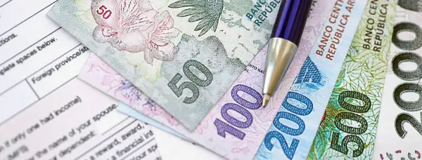 Arjantin pezosu. Büyük miktarda para. Masada, kalem ve vergi formları var.