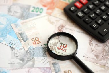 Brezilya reais banknotları ve büyüteçli hesap makinesi. Mevcut Brezilya gerçek para faturaları ve loupe ile calc büyük miktarda masada yatıyor. Brezilya 'da vergilendirme ve para konsepti