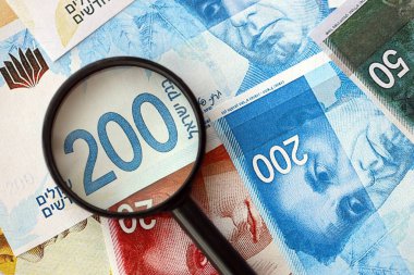 Israel New Shekels banknotları ve büyüteç. Şu anki İsrail 'in yüksek meblağlı faturaları masanın üzerinde yatıyor. İsrail 'de mali izleme ve vergilendirme kavramı