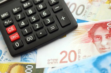 Israel New Shekels banknotları ve hesap makinesi. Mevcut İsrail para faturaları ve kalibreleri büyük miktarda masada yatıyor. İsrail 'de vergilendirme ve para kavramı