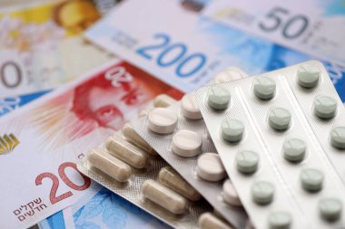 Israel New Shekels banknotları ve ilaç hapları. Mevcut İsrail para ve uyuşturucu faturaları büyük miktarda masada yatıyor. İsrail 'de ilaç ve eczane kavramı