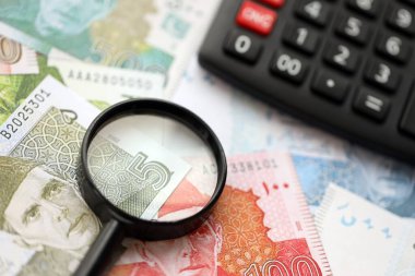 Pakistan banknotları ve büyüteçle hesap makinesi. Mevcut Pakistan para faturaları ve loupe ile calc büyük miktarda masada yatıyor. Pakistan 'da vergi ve para sayımı kavramı