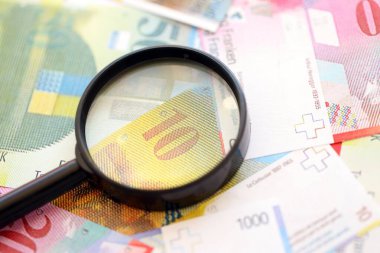 İsviçre frangı banknotları ve büyüteç. İçinde loupe olan şu anki para banknotları büyük miktarda masada yatıyor. İsviçre 'de mali izleme ve vergilendirme kavramı