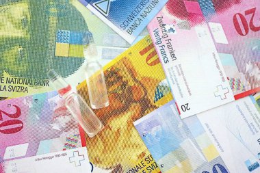 İsviçre frangı banknotları ve ilaç şişeleri. Mevcut para faturaları ve enjeksiyon dozu büyük miktarda masada yatıyor. İsviçre 'de ilaç ve aşı kavramı