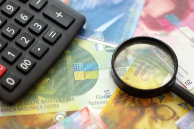 İsviçre frangı banknotları ve büyüteçli hesap makinesi. Mevcut para faturaları ve loupe ile calc büyük miktarda masada yatıyor. İsviçre 'de vergilendirme ve iş kavramı