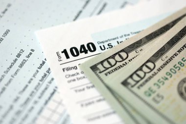 Yüz dolarlık banknotlar ve 1040 bireysel gelir vergisi iade formu yakın çekim. Çok az Amerikan doları ve Birleşik Devletler vergisi yok. ABD 'de vergi ödeme ve muhasebe kavramı