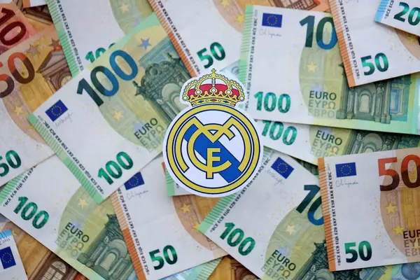 KYIV, UKRAINE - 23 Şubat 2025 Real Madrid CF futbol kulübü rozeti büyük miktarda EURO para banknotlarının üzerinde yatıyor