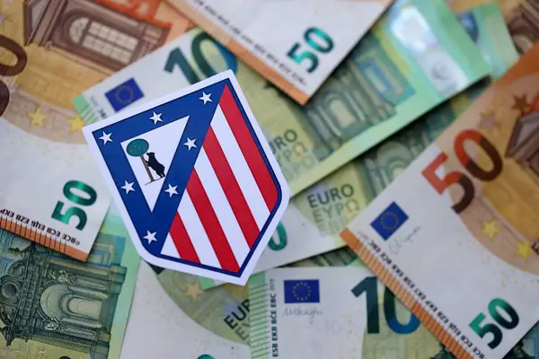 KYIV, UKRAINE - 23 Şubat 2025 Atletico de Madrid futbol kulübü rozeti büyük miktarda EURO para banknotlarının üzerinde yatıyor