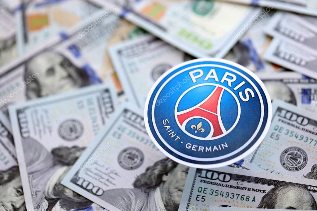 KYIV, UKRAINE - FEBRUARY 23, 2025 Paris Saint Germain FC football club badge lies on big amount of hundred US dollar bills
