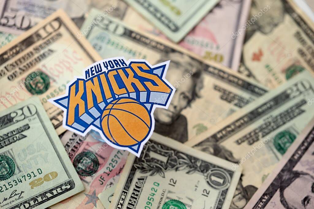 KYIV, UKRAINE - FEBRUARY 23, 2025 New York Knicks basketball team badge lies on big amount of US dollar bills close up