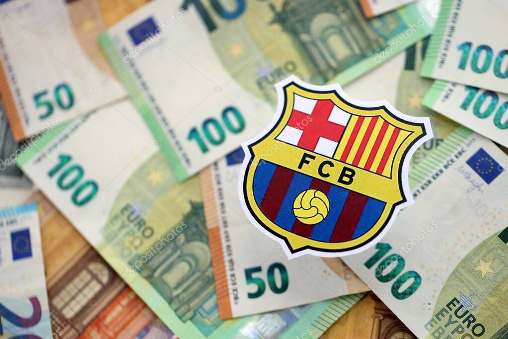KYIV, UKRAINE - FEBRUARY 23, 2025 FC Barcelona football club badge lies on big amount of hundred EURO money bills