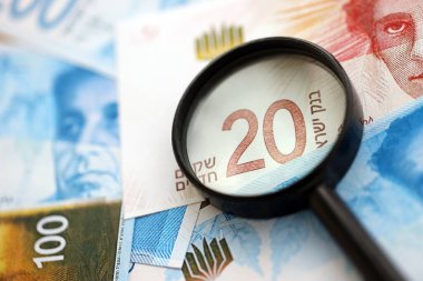 Israel New Shekels banknotları ve büyüteç. Şu anki İsrail 'in yüksek meblağlı faturaları masanın üzerinde yatıyor. İsrail 'de mali izleme ve vergilendirme kavramı