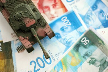Israel New Shekels banknotları ve oyuncak tankı. İsrail 'in şu anki para ve tankı büyük miktarda masanın üzerinde duruyor. İsrail 'de ordu fonları ve silah satışları kavramı