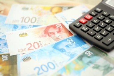Israel New Shekels banknotları ve hesap makinesi. Mevcut İsrail para faturaları ve kalibreleri büyük miktarda masada yatıyor. İsrail 'de vergilendirme ve para kavramı