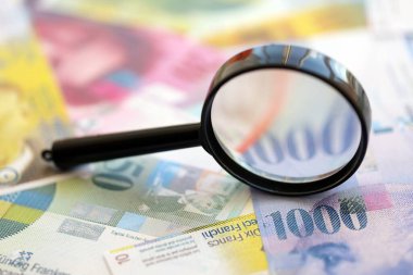 İsviçre frangı banknotları ve büyüteç. İçinde loupe olan şu anki para banknotları büyük miktarda masada yatıyor. İsviçre 'de mali izleme ve vergilendirme kavramı