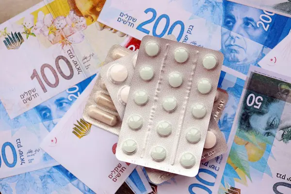 Israel New Shekels banknotları ve ilaç hapları. Mevcut İsrail para ve uyuşturucu faturaları büyük miktarda masada yatıyor. İsrail 'de ilaç ve eczane kavramı